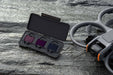 Set of three small devices in a black case on a stone surface with a drone in the background.