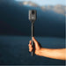 Hand holding a DJI action camera on a pole with a blurred natural background